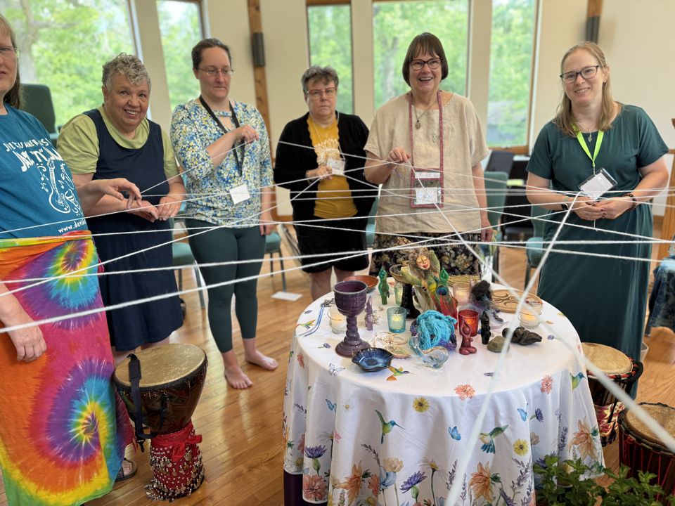 several women standing around a table, each holding a part of a long strand of yarn