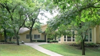 beige building with lots of windows and a long concrete walkway, surrounded by green trees
